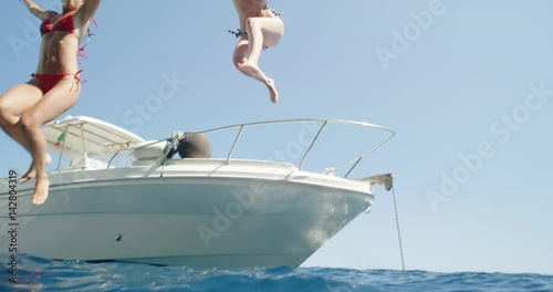Women jumping off boat into ocean two girls jump into clear blue water from sailboat enjoying active lifestyle summer holiday travel vacation adventure