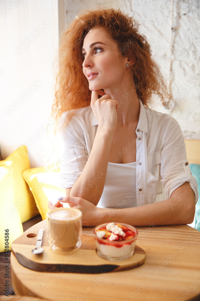 Amazing redhead young lady sitting in cafe while eating dessert. Amazing redhead young lady sitting in cafe while eating dessert.