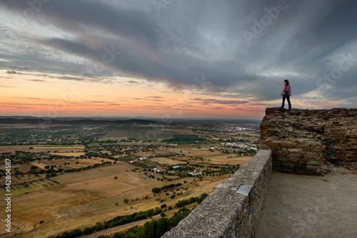 Turista a contemplar o Pôr do Sol no castelo da vila mediaval de Monsaraz, Alentejo, Portugal
