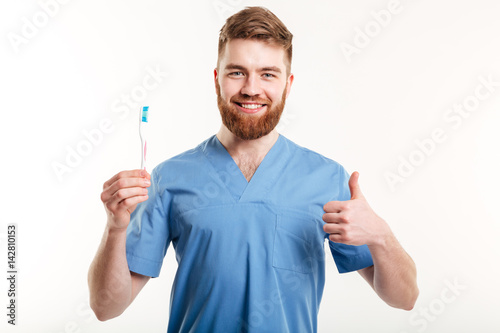 Smiling male dentist holding toothbrush and showing thumbs up