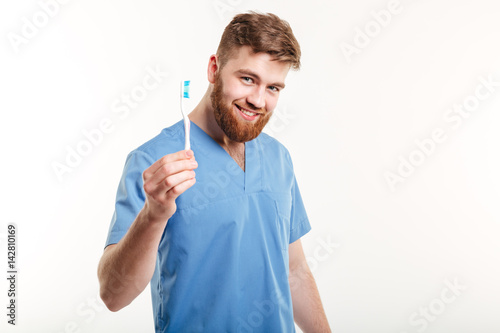 Smiling young male dentist holding toothbrush and looking at camera