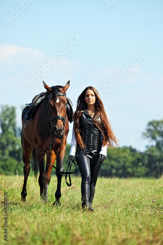 Young romantic girl in antique leather leggings and corset leading saddle horse 