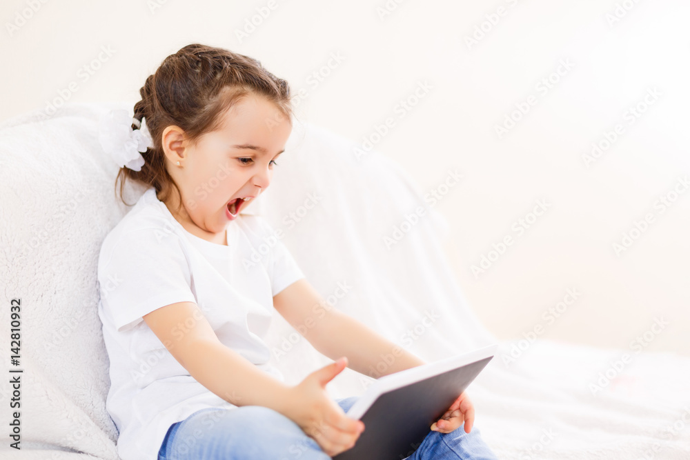 Little girl playing with a digital tablet at home on a sofa Little girl playing with a digital tablet at home on a sofa