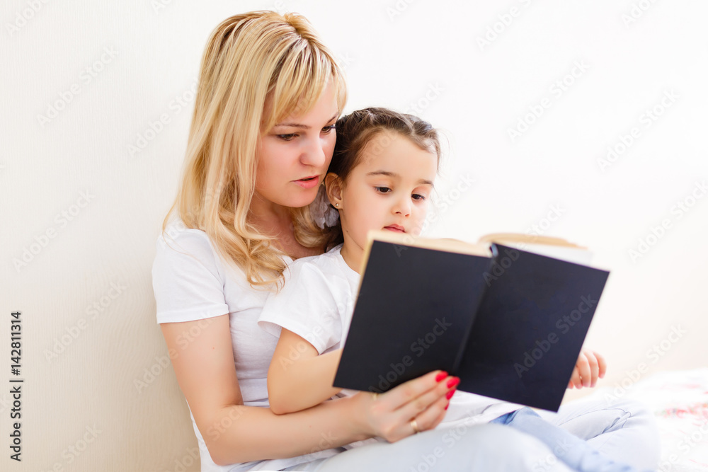 happy family mother child daughter little girl reading a book by the window happy family mother child daughter little girl reading a book by the window