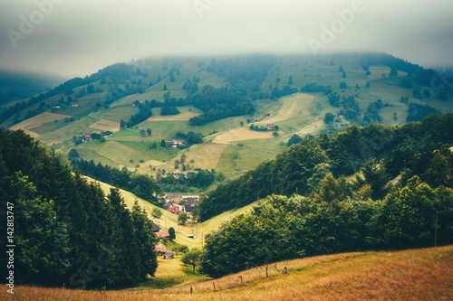 Dreamy mountain landscape with picturesque village houses covered in fog. Germany, Muenstertal, Black forest. Travel background.