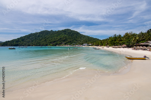 Paradise beach view with huts and small boat and a forested hill background. Perhentian Kecil, Malaysia.