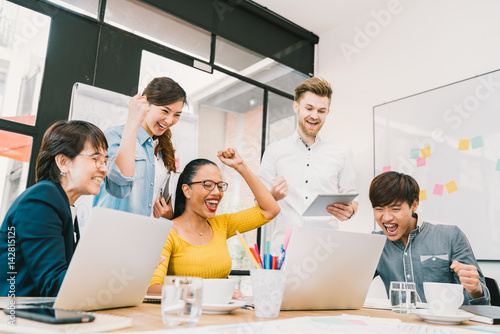 Multiethnic diverse group of coworkers celebrate together with laptop and tablet. Creative team  casual business colleague  college student at modern office. Startup  teamwork  success project concept