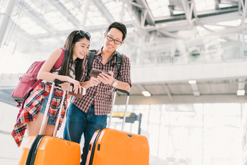 Asian couple travelers using smartphone checking flight or online check-in at airport, with passport and luggage. Air travel or mobile phone technology concept