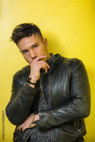Handsome white asian young man wearing black leather jacket standing on yellow background against wall in studio shot © theartofphoto