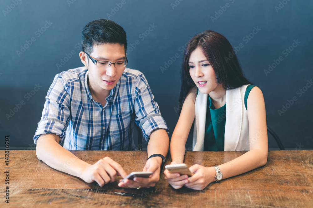 Young Asian couple, college students, or coworkers using smartphone together at cafe, modern lifestyle with gadget technology or love and relationship concept Young Asian couple, college students, or coworkers using smartphone together at cafe, modern lifestyle with gadget technology or love and relationship concept