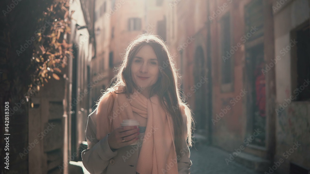 Portrait of young smiling woman looking at camera. Happy attractive girl standing in morning street, doing up hair.