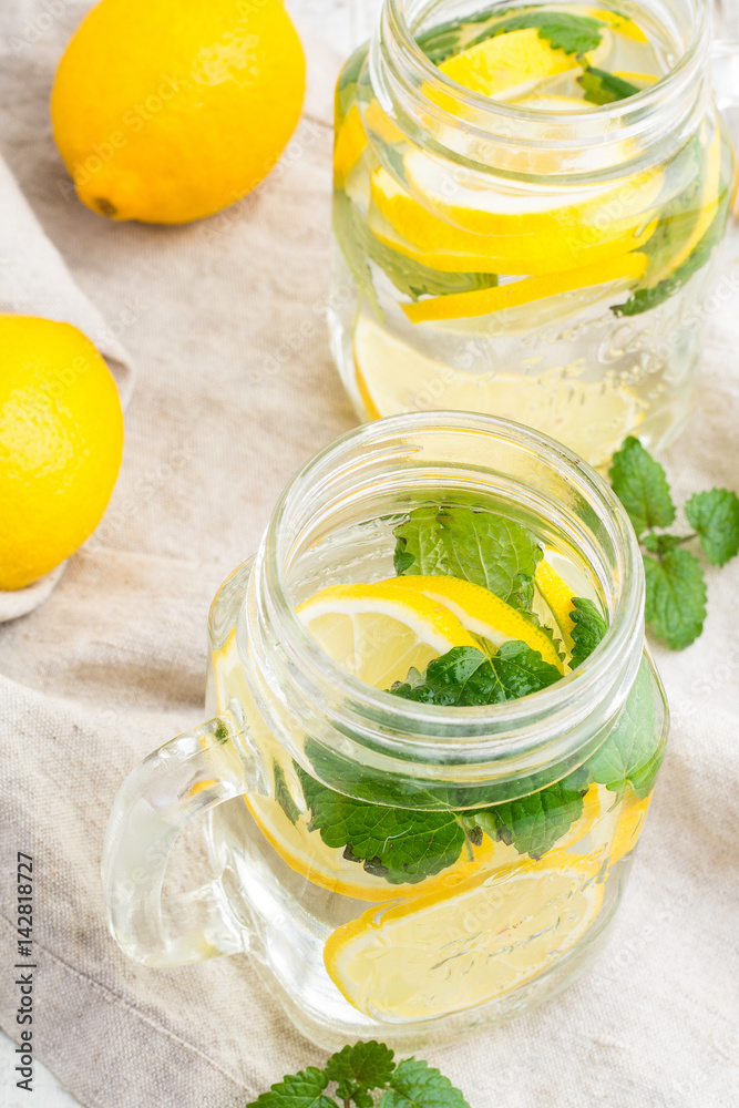 Water with lemon and mint in a glass mug on a tablecloth close-up.