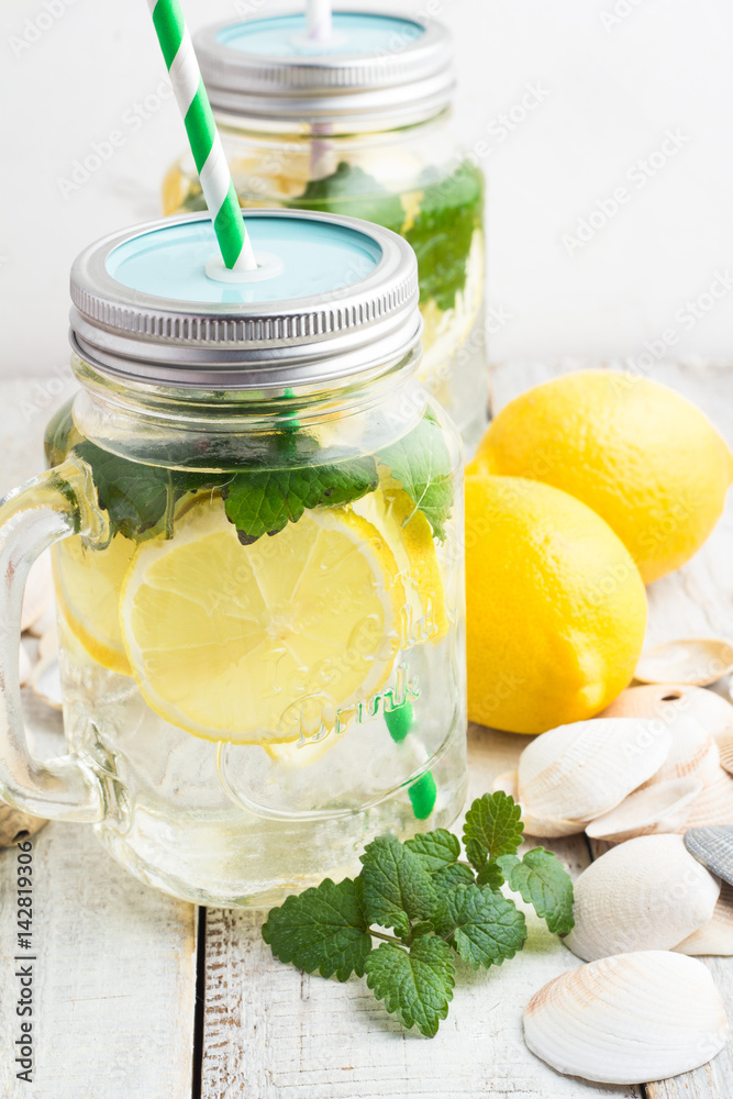 Water with lemon and mint in a glass mug with a lid and a straw.