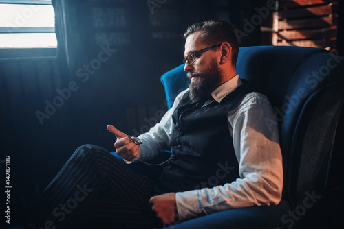 Man sitting in armchair, looking at pocket watch
