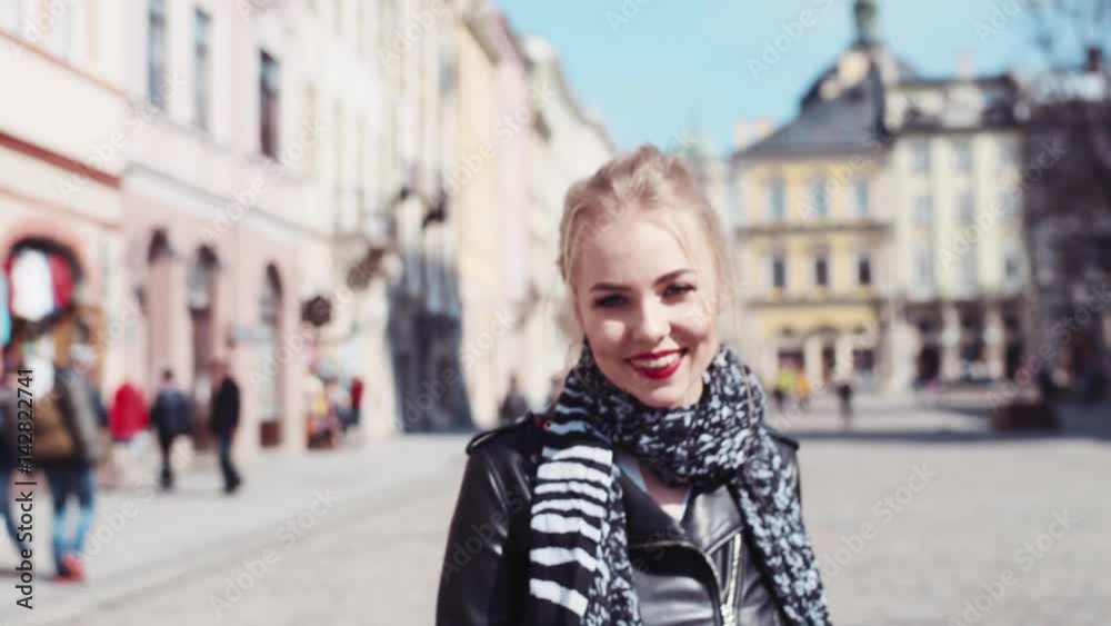 Happy young woman in an elegant wear walking in Lviv’s center, turns to camera and smiles. Being happy, sunny day. Positive mood. Old buildings on the background. Happy young woman in an elegant wear walking in Lviv’s center, turns to camera and smiles. Being happy, sunny day. Positive mood. Old buildings on the background.