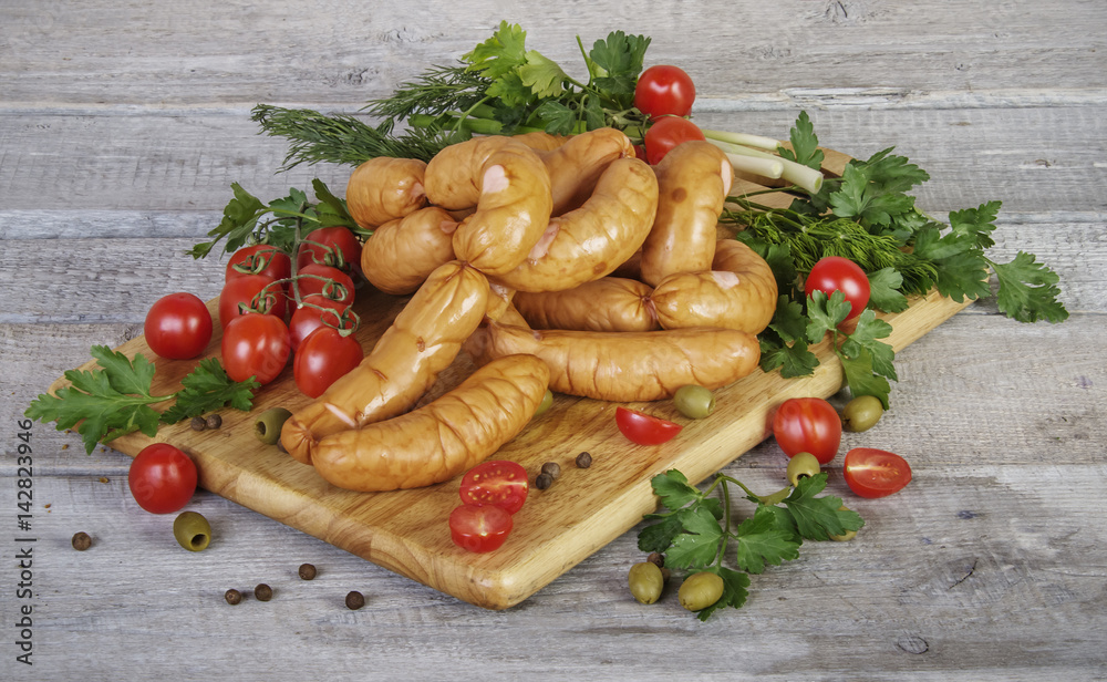 homemade sausages on wooden cutting board with parsley, dill, onion, tomatoes and olives