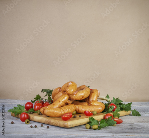 old paper background with homemade sausages, parsley, dill, onion, tomatoes and olives on wooden cutting board photo