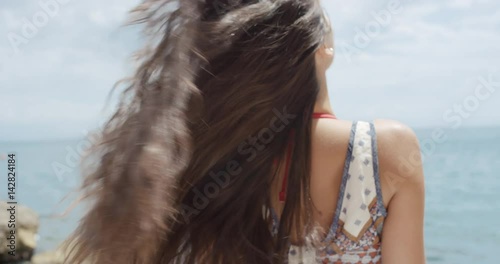 Rear view portrait of Beautiful Young Woman flicking hair blowing in wind on tropical beach slow motion from behind