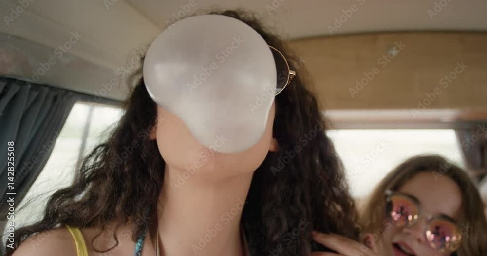 Portrait Beautiful African American Teenage girl blowing bubblegum candy bubbles having fun at festival in camper van on road trip adventure