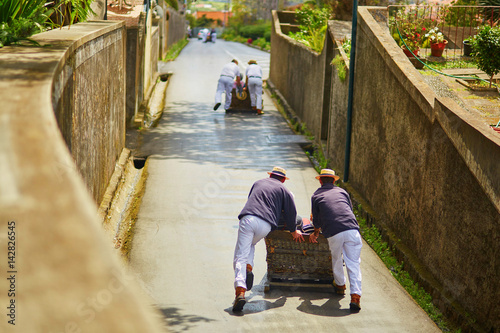 Fotografie Toboggan riders pushing wooden sledge downhill in Funchal, Madeira island, Portu