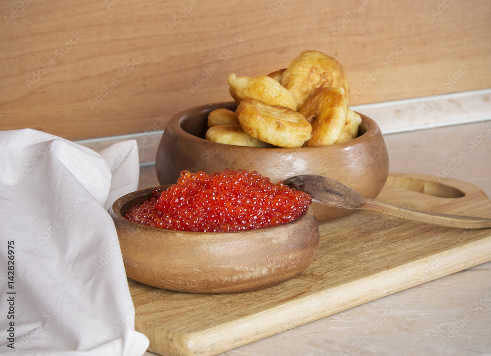 Wooden background with salmon caviar and pancakes in wooden dishes Russian cuisine