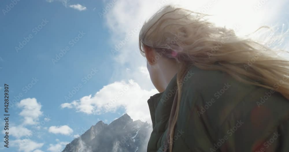 Close up portrait of Woman Climber at top of mountain in nature with blonde hair blowing in wind above the clouds view Hiker Girl trekking in Norway Slow Motion