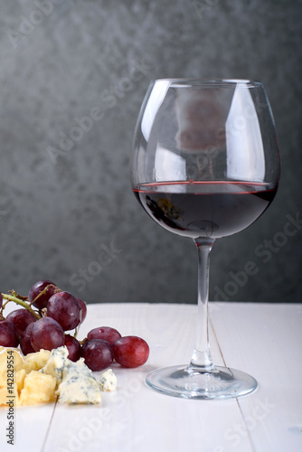 A glass of red wine, a bunch of grapes and cheese on the table