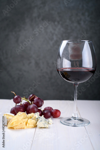 A glass of red wine, a bunch of grapes and cheese on the table
