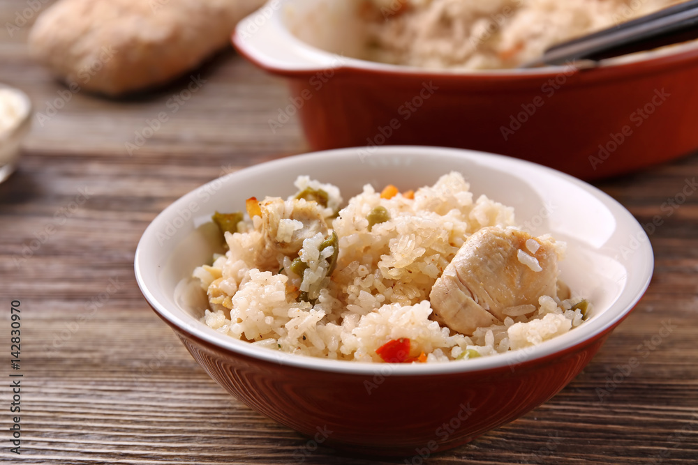 Delicious rice with chicken and vegetables in plate on wooden table Delicious rice with chicken and vegetables in plate on wooden table