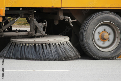 Yellow urban sweeper cleans road from dirt with a round brush in the spring.