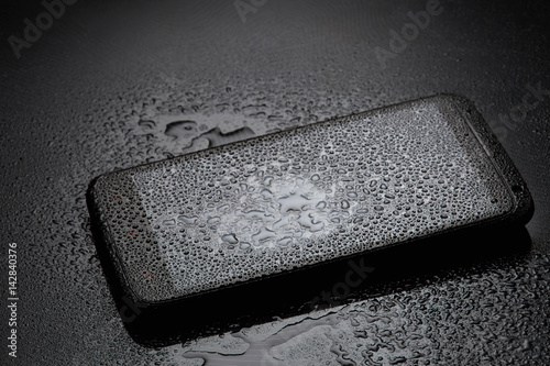Smartphone with water drops on dark background