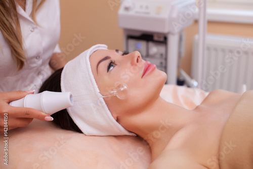 Photos The doctor-cosmetologist makes the procedure Microcurrent therapy of the facial skin of a beautiful, young woman in a beauty salon