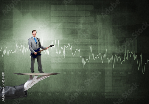 Businessman on metal tray playing electric guitar against graphs background