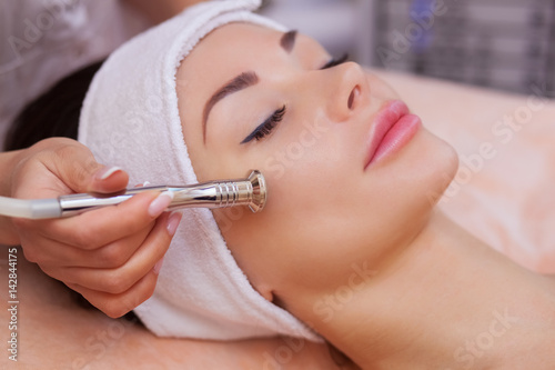 The doctor-cosmetologist makes the procedure Microdermabrasion of the facial skin of a beautiful, young woman in a beauty salon.Cosmetology and professional skin care.