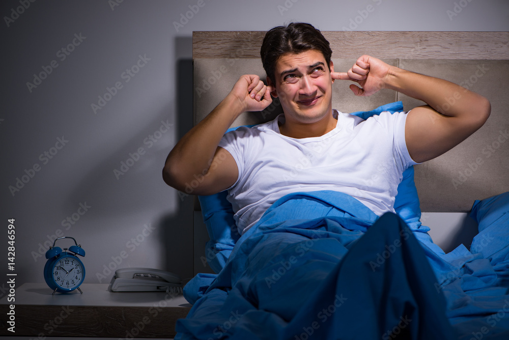 Young man struggling from noise in bed - obrazy, fototapety, plakaty 