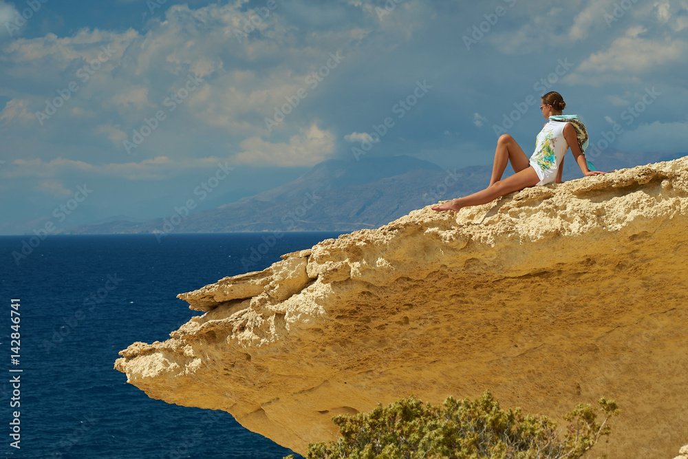 A girl is sitting on the cliff and observing the sea.