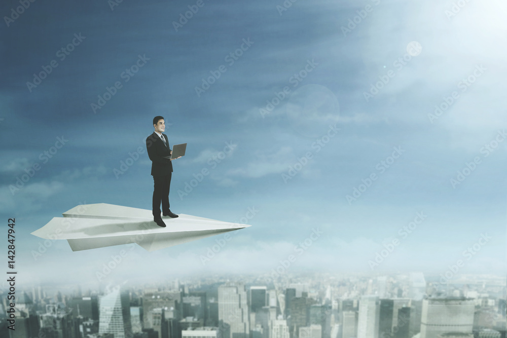 Businessman with laptop stands on paper plane