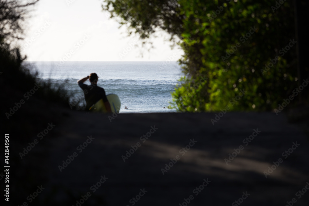 A surfer with surfboard under arm checks the morning surf at a scenic beach in Australia.