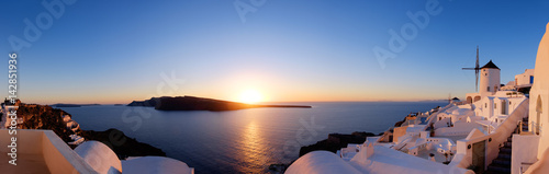 Traditional apartments and windmills in Oia village on a sunset, panoramic image
