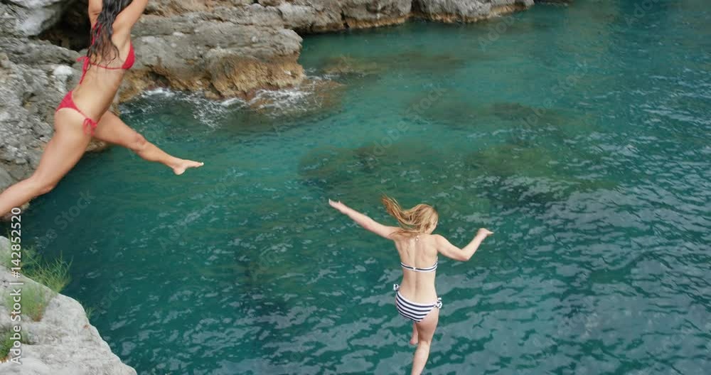 Athletic women jumping from cliff into sea best friends enjoying European summer holiday travel vacation adventure in Amalfi Coast Italy