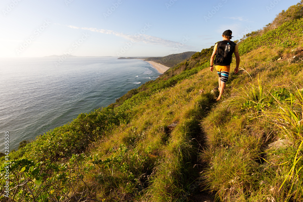 A hiker looking at a beautiful coastline view over the sea during a bright summer morning as he walks on a grassy coastal trail in Australia.