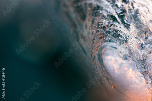 Abstract, close up water shot of the inside of a breaking, barrelling wave as golden sunset light filters through.