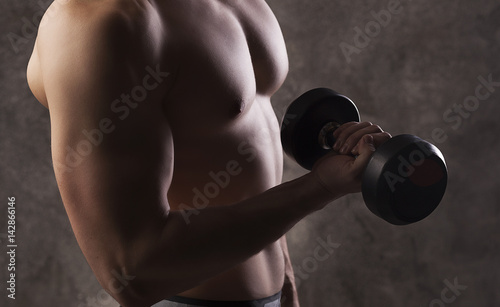 Young strong male athlete demonstrating his torso, athlete with dumbbells