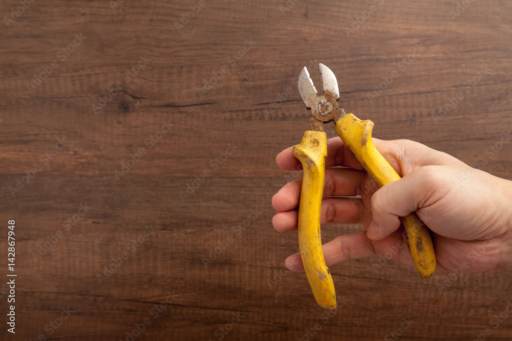 a man hold a yellow cutting plier on wooden background.