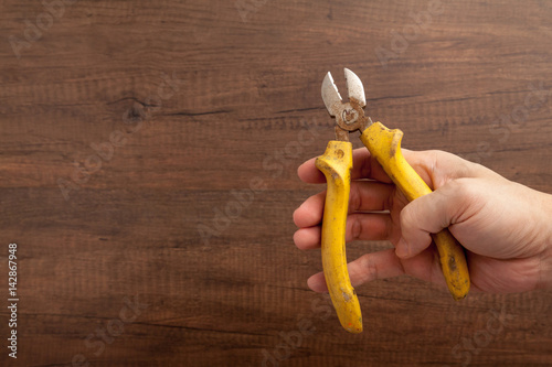 a man hold a yellow cutting plier on wooden background.