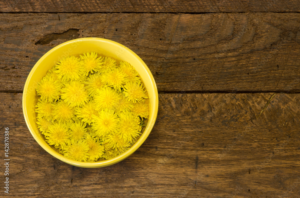A bowl of dandelion flowers on a rustic wood background with room for text. A bowl of dandelion flowers on a rustic wood background with room for text.