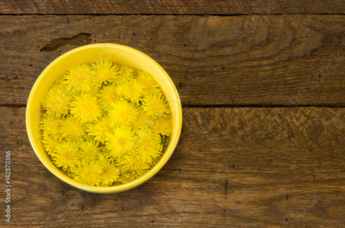 A bowl of dandelion flowers on a rustic wood background with room for text. photo