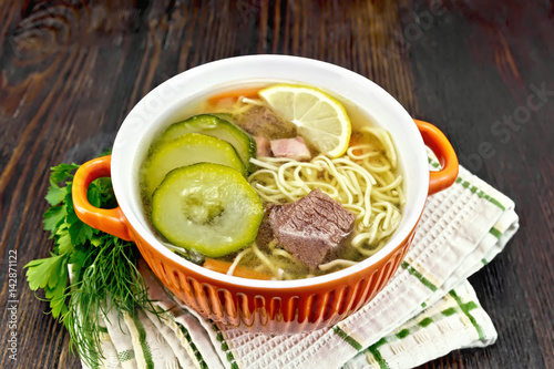 Soup with zucchini and noodles in red bowl on wooden board