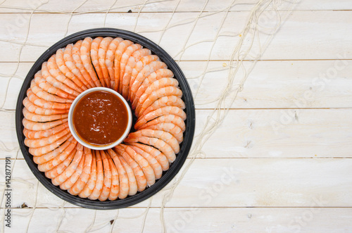 Shrimp ring with seafood cocktail sauce on a white rustic plank surface with fish net