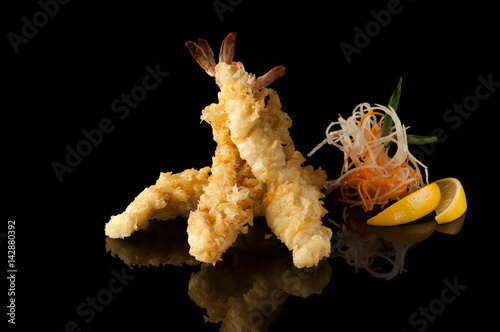 shrimp in tempura with lemon slices and salad on a black background with reflection